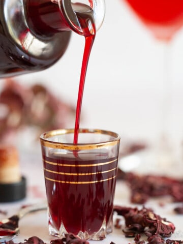 Close up of hibiscus syrup being poured from a bottle into a glass.