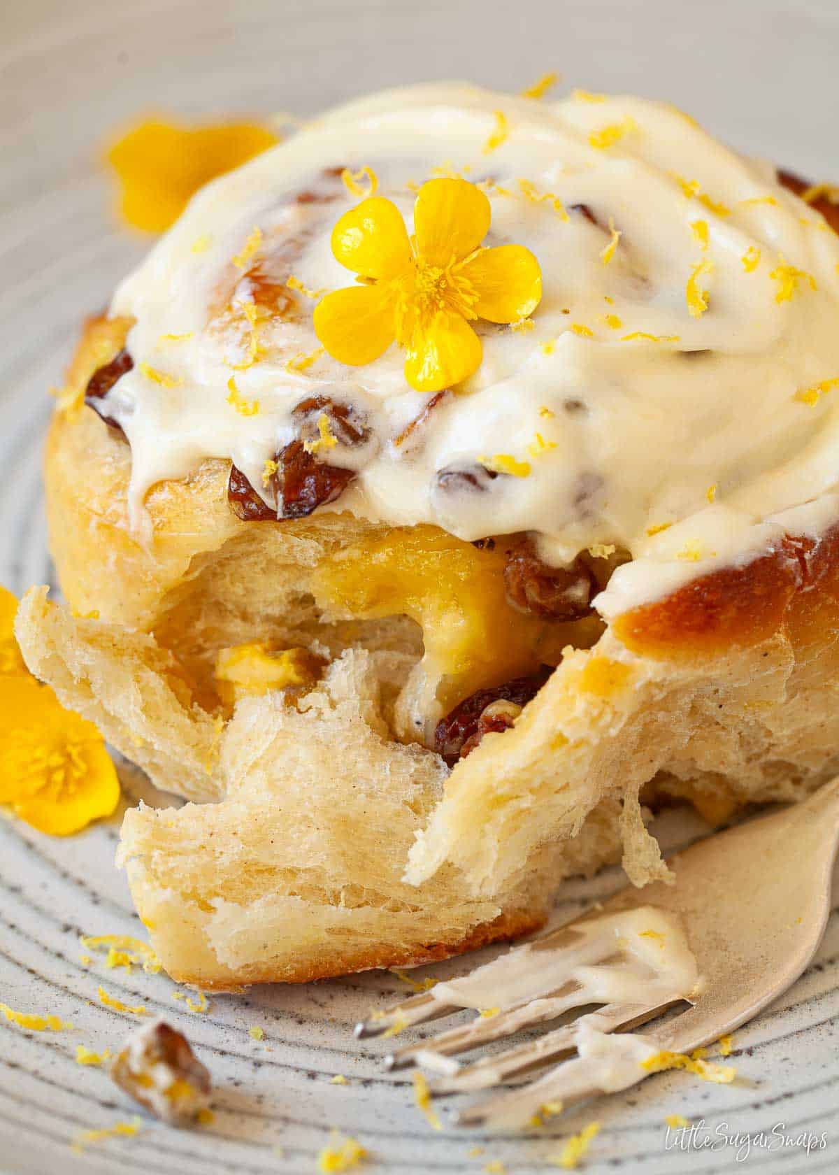 Close up of a lemon curd bun with sultanas and cream cheese frosting.