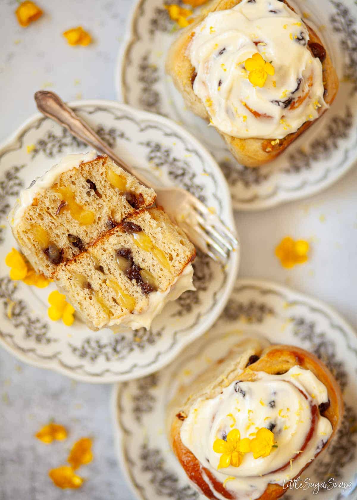 Lemon rolls on plates, one has been cut open to reveal the lemon curd and sultana filling.