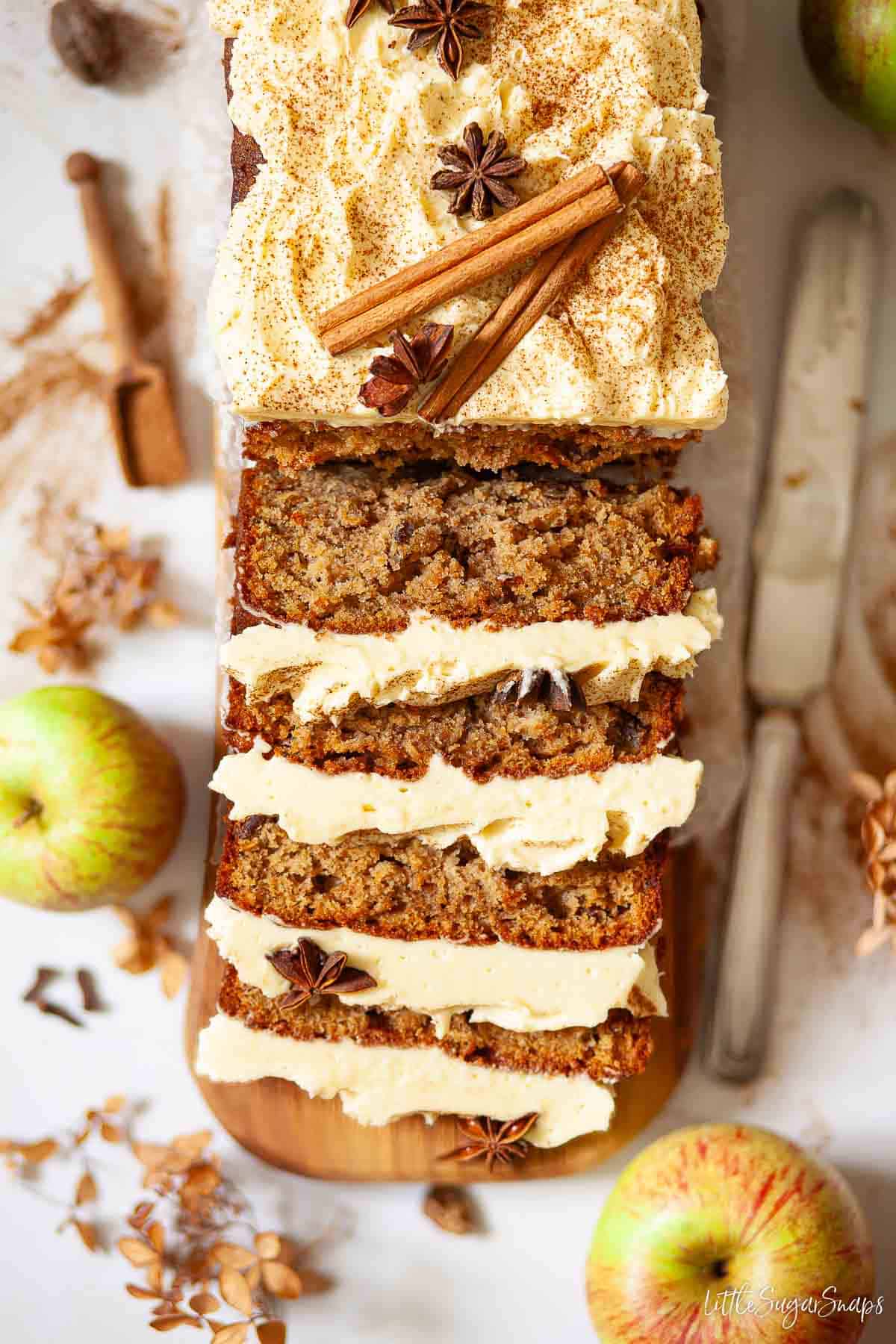 A spiced apple loaf cake topped with buttercream, cinnamon sticks and star anise. It has been partially sliced.