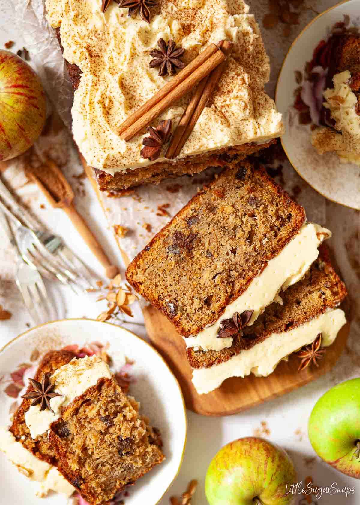 Apple loaf cake topped with buttercream, cinnamon sticks and star anise. It has been partially sliced.