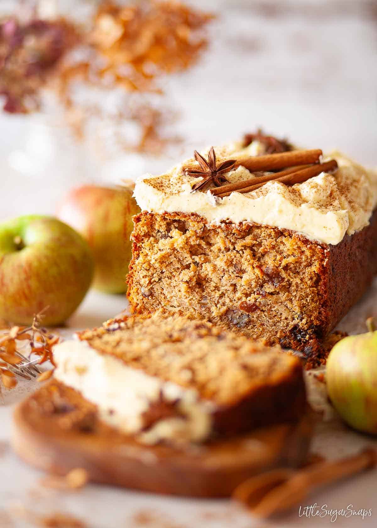 Spiced apple loaf cake topped with buttercream, cinnamon sticks and star anise. It has been partially sliced.