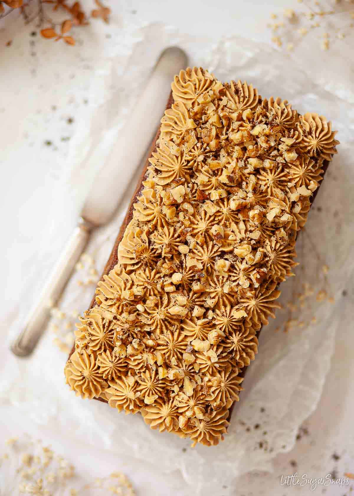 Overhead view of a coffee loaf cake topped with piped buttercream and chopped nuts.