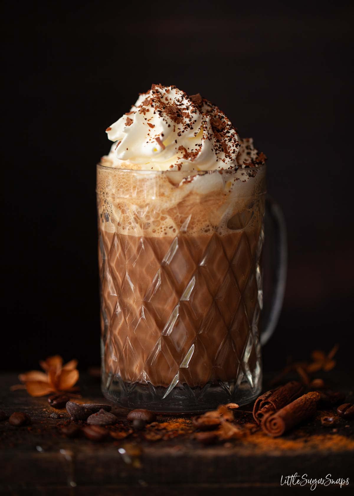 A chocolate coffee drink in a patterned glass much topped with whipped cream, chilli and grated chocolate.