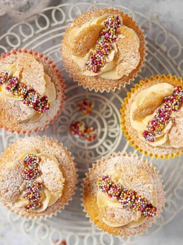 Five small butterfly style cakes on a wire stand. They are topped with candy pieces.
