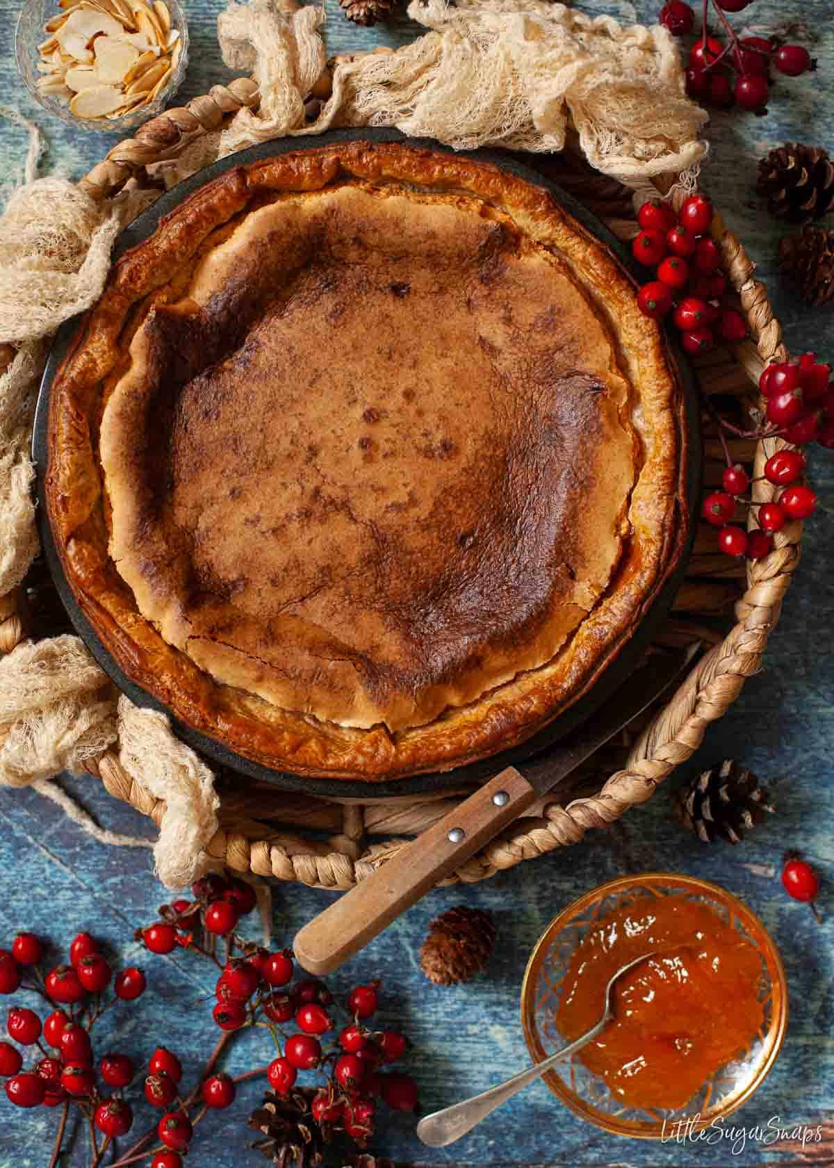 A whole Bakewell pudding sitting in a basket in aqn autumnal setting.