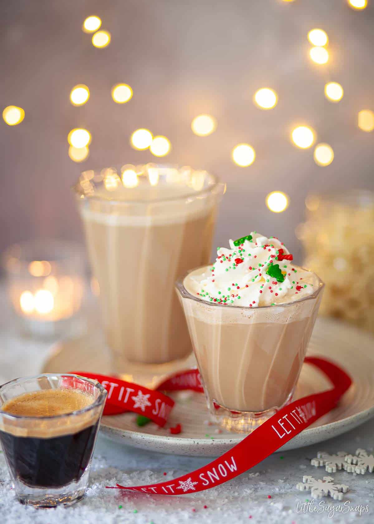 Peppermint coffee drinks served in glasses. One is topped with whipped cream and sprinkles.