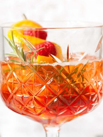Close up of a winter spritz with sloe gin, Aperol and rosemary garnish.