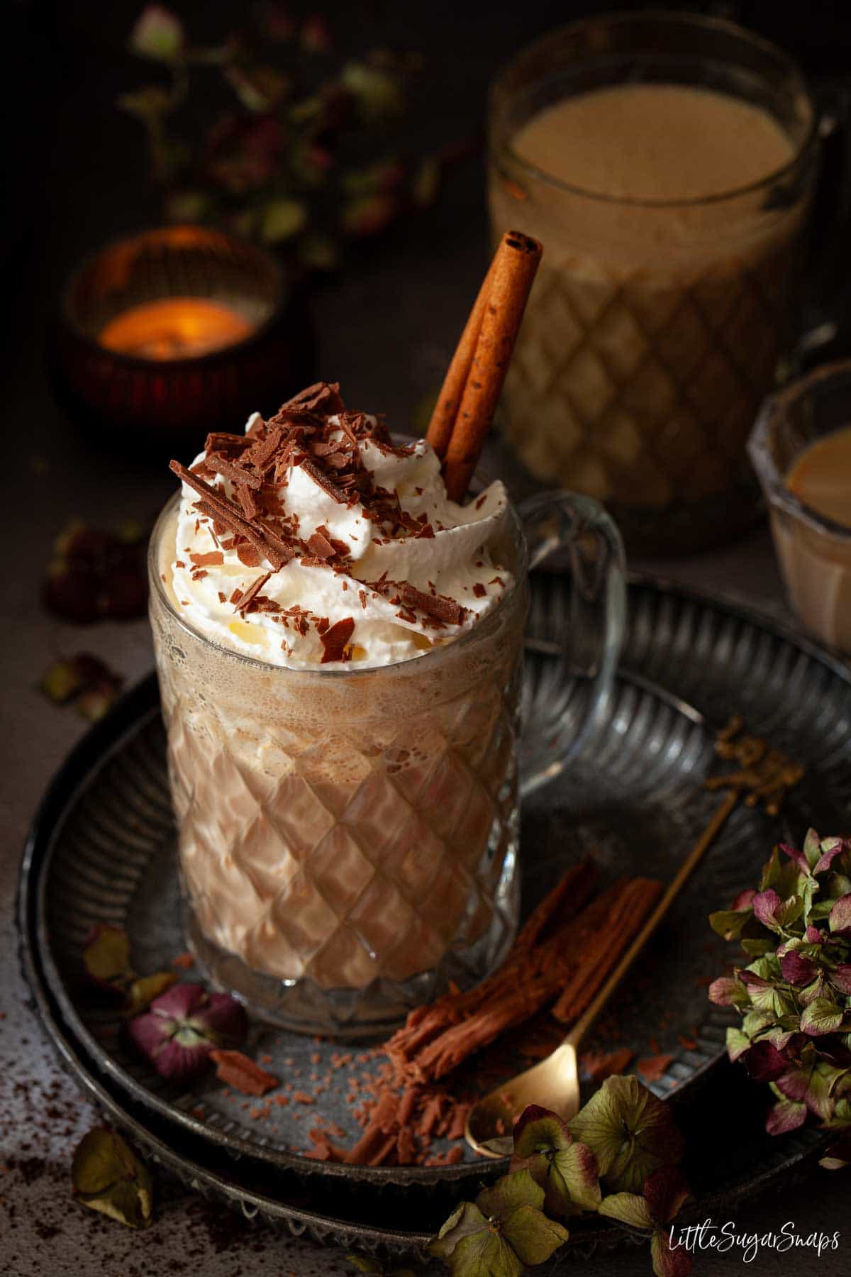 An Irish latte on metal plates with whipped cream, grated chocolate and cinnamon stick garnishes.