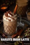 Labelled warm Baileys coffee drink in a glass with cream, chocolate flakes and cinnamon stick.