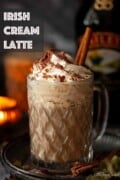 Labelled warm Baileys coffee drink in a glass with cream, chocolate flakes and cinnamon stick.