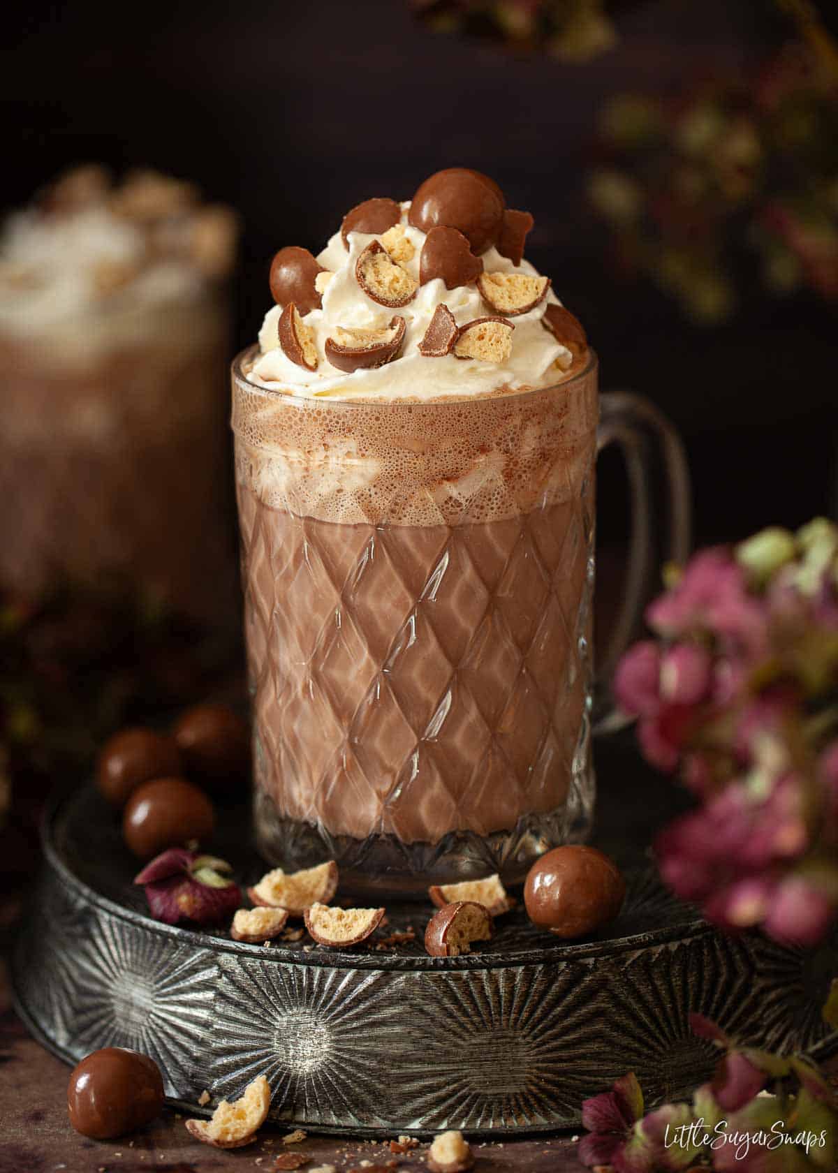 A glass holding a warm chocolate drink topped with cream and crushed honeycomb chocolates.