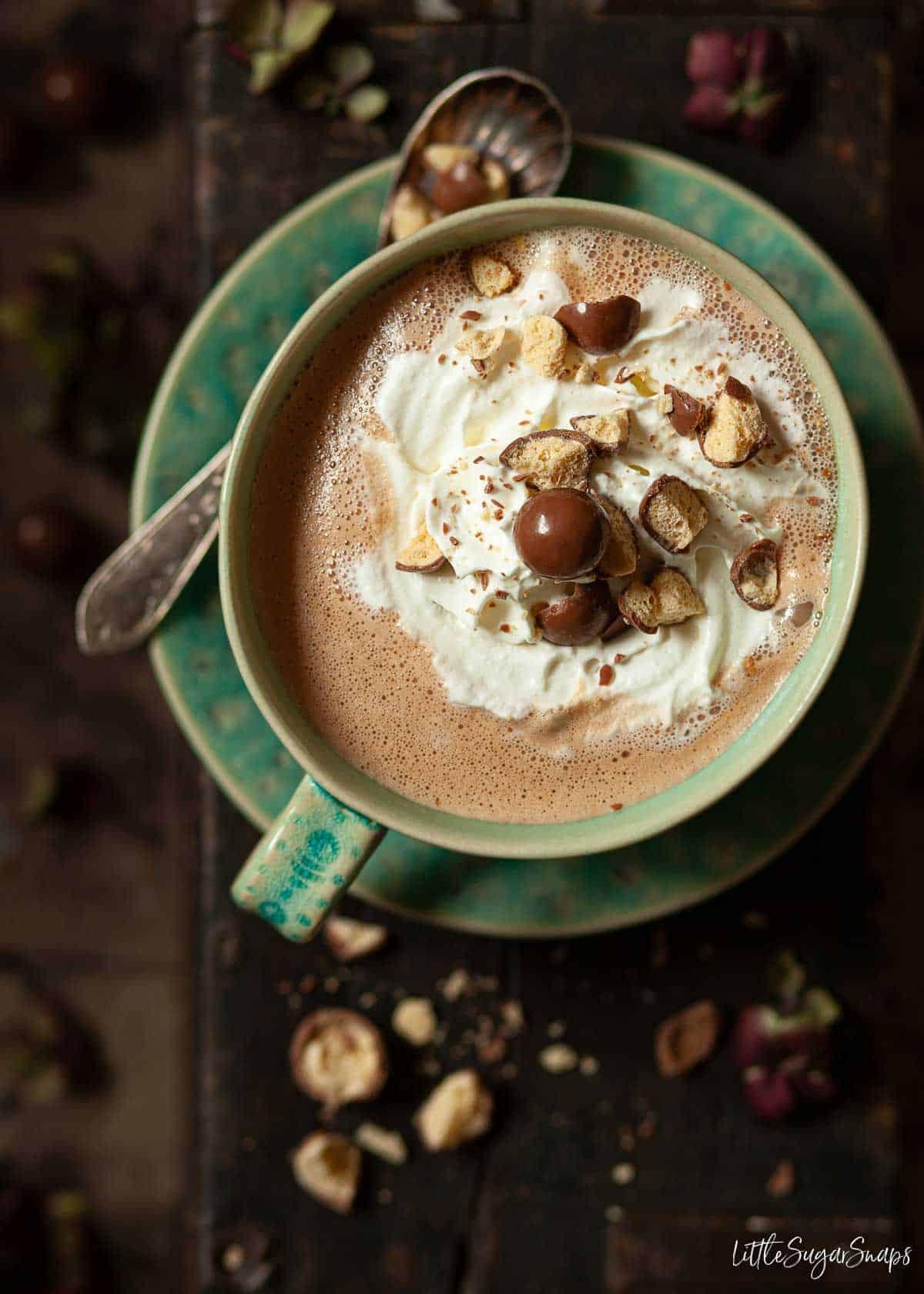 A warm chocolate drink in a blue cup topped with whipped cream and honeycomb chocolate balls.