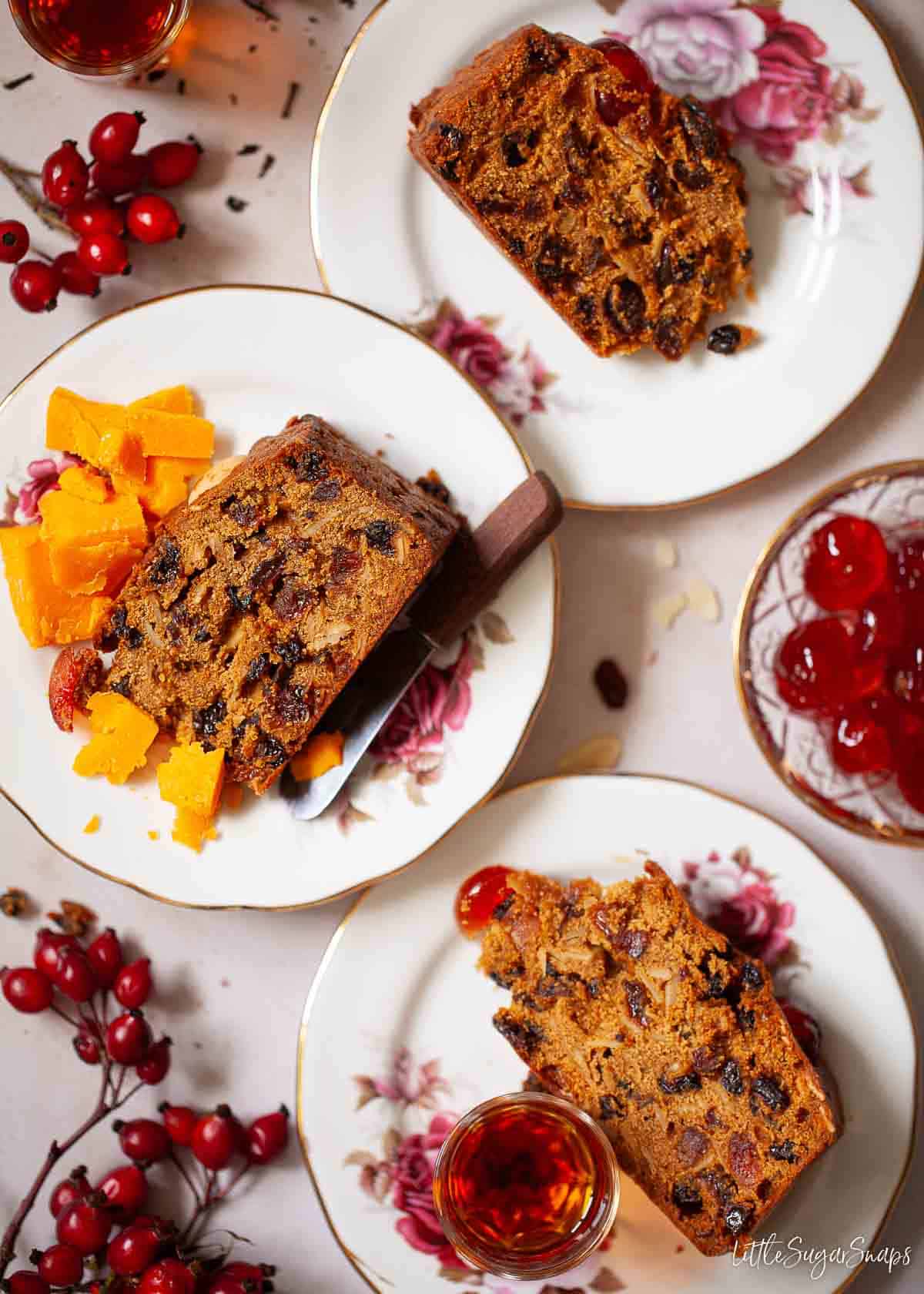 Three slices of Melton Hunt cake on plates with cheese and rum served alongside.