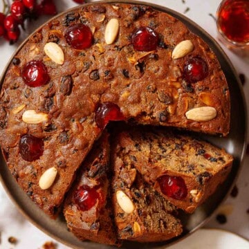 Sliced rum fruit cake with glacé cherries and almonds on the top.