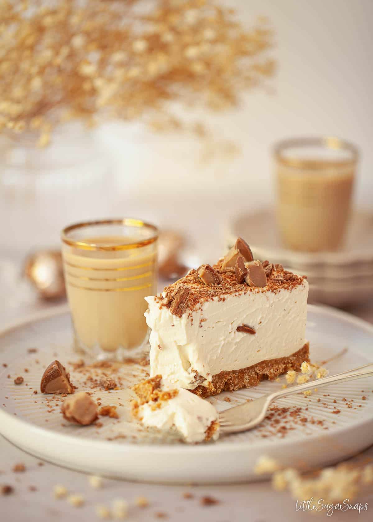 A slice of Baileys cheesecake with a piece scooped onto a fork lying on the plate alongside it.