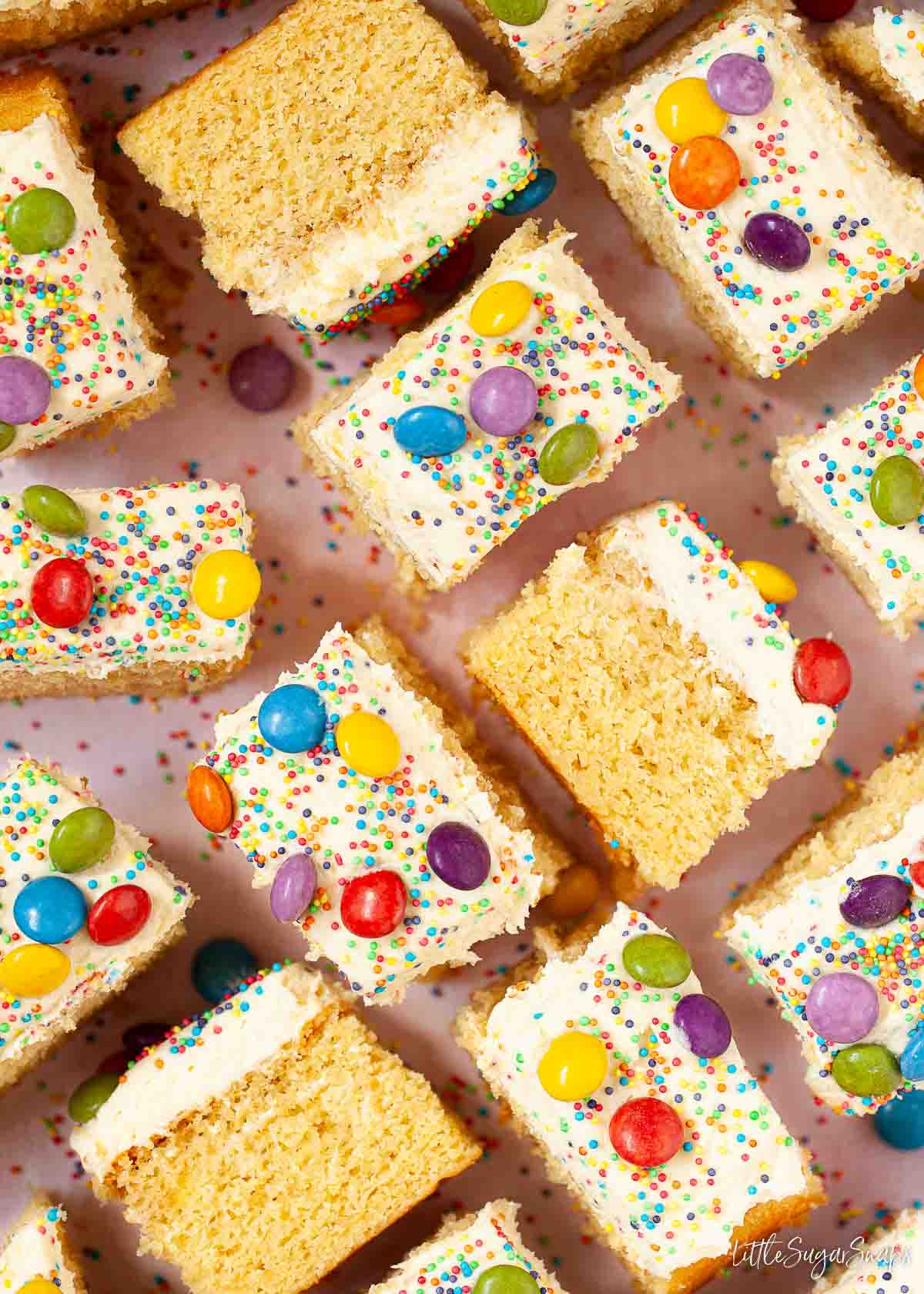 Squares of vanilla tray bake topped with vanilla buttercream, sprinkles and colourful chocolate candy.