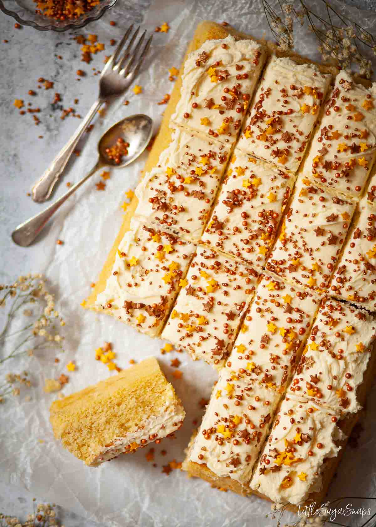 Sliced up sponge tray bake cake topped with buttercreamand gold & bronze sprinkles.