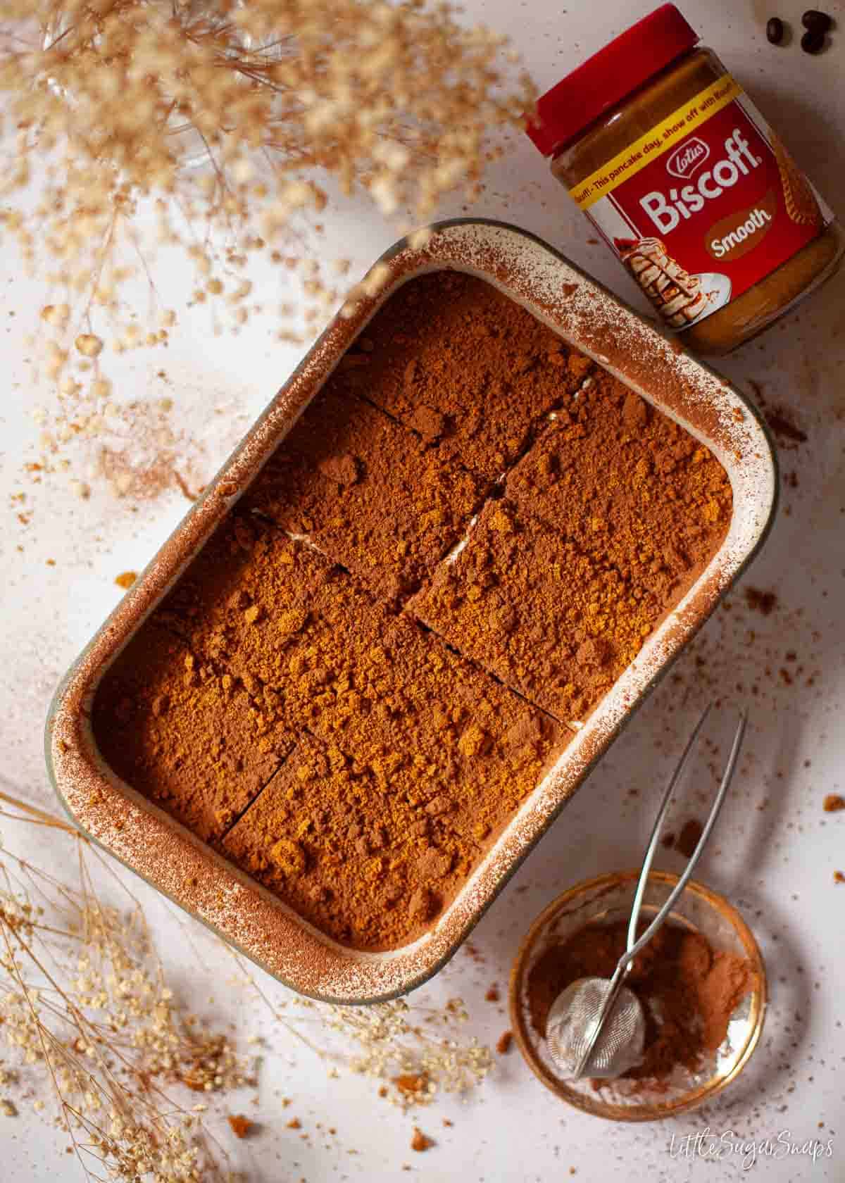 A bowl of Biscoff tiramisu with portions marked out on the top and a jar of cookie butter alongside it.