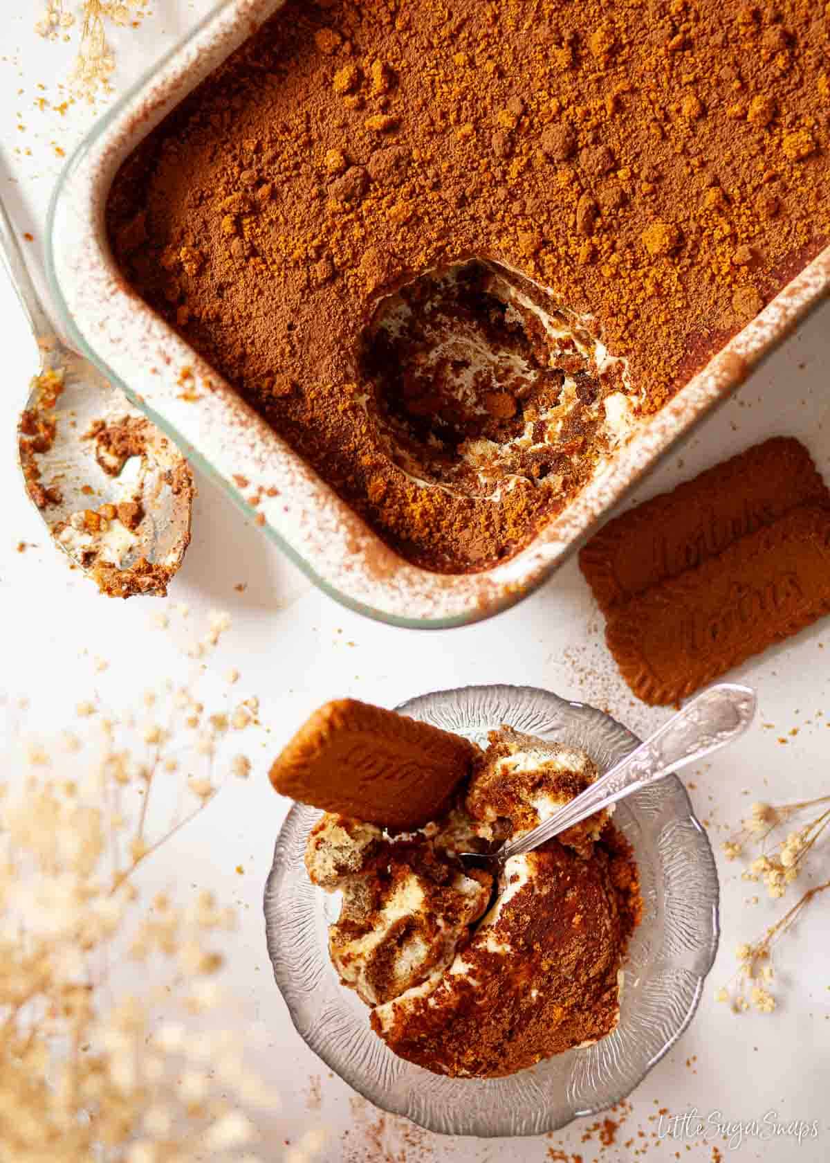 A speculoos tiramisu with a portion scooped out into a glass dessert bowl.