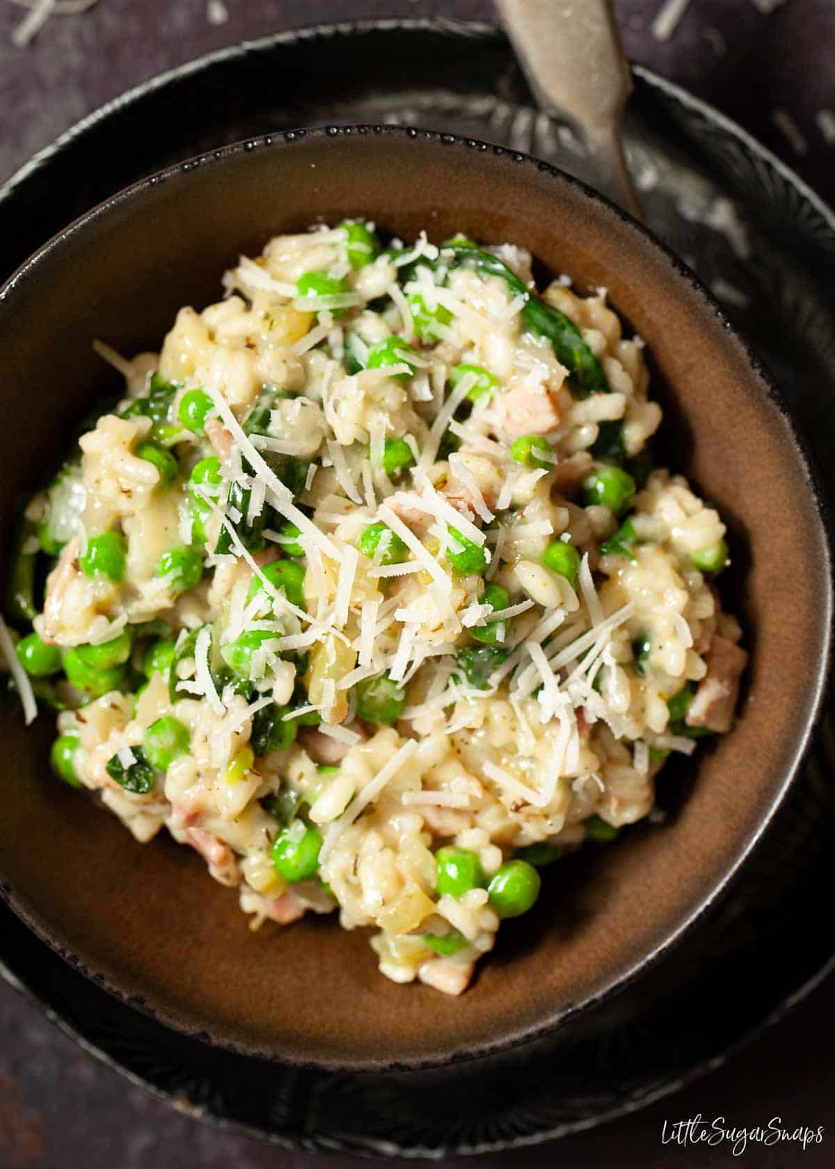 A bowl of bacon and pea risotto garnished with grated parmesan cheese.