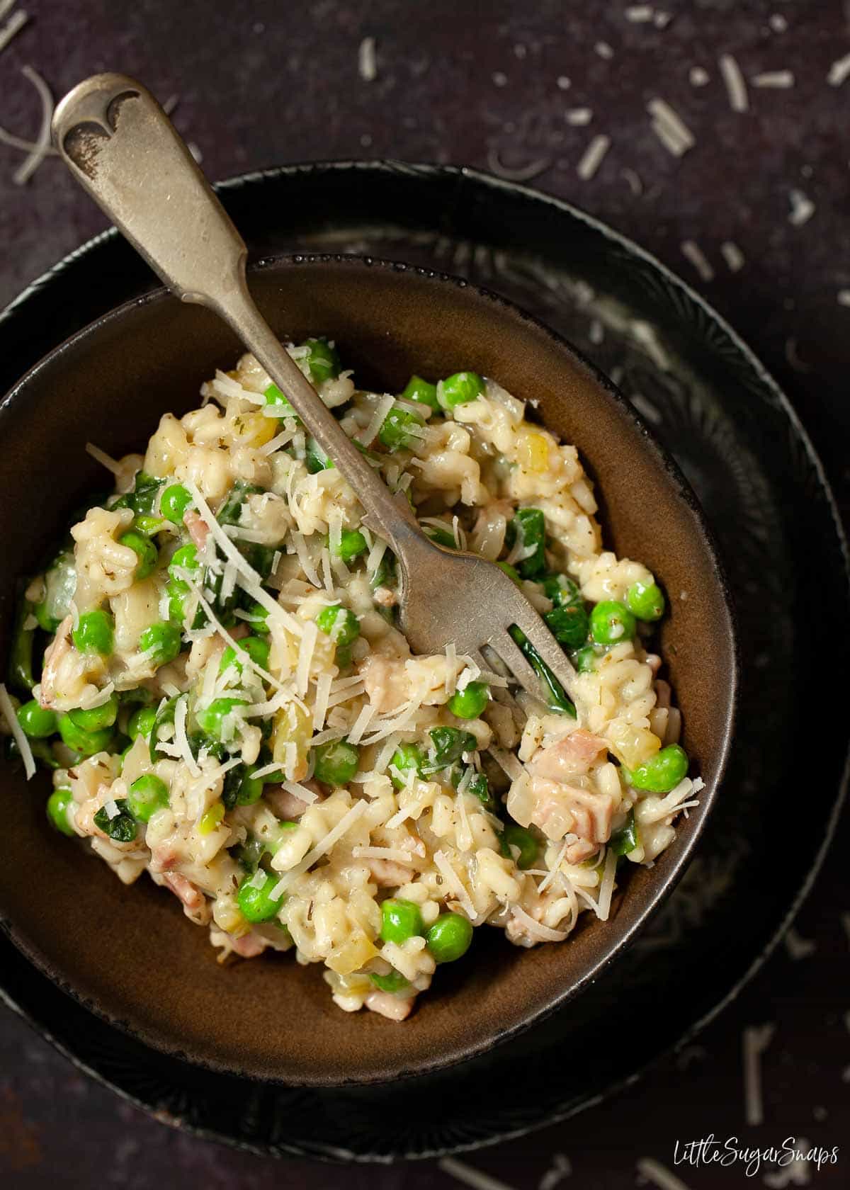 A bowl of pea risotto with a fork pushed into the rice.