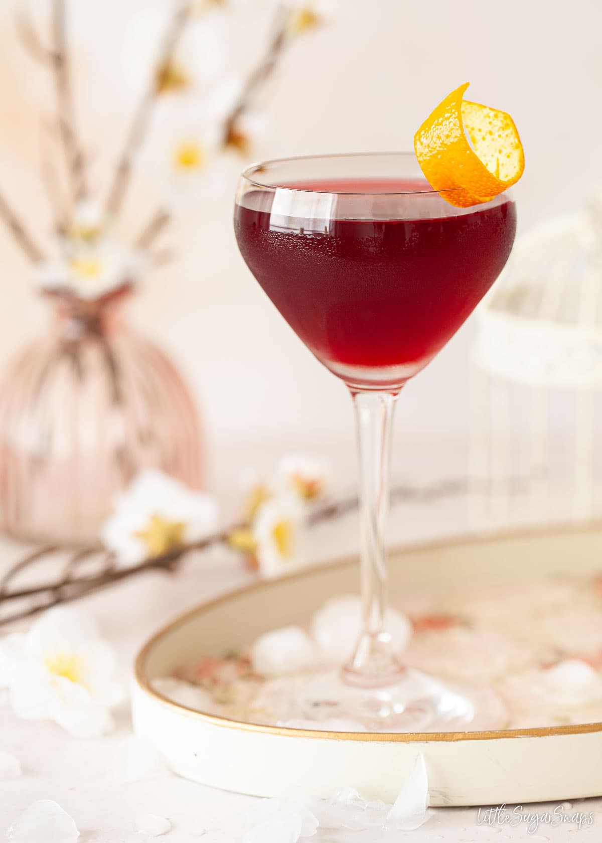 A creme de cassis cocktail in a Nick and Nora glass garnished with orange zest.