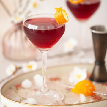 Close up off a creme de cassis cocktail garnished with orange zest.