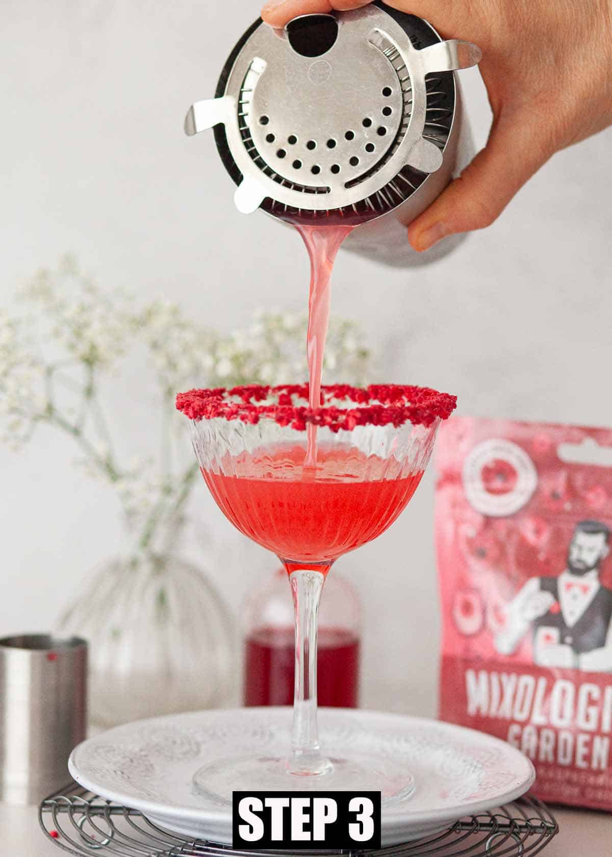 A red fruit cocktail being poured into a serving glass.