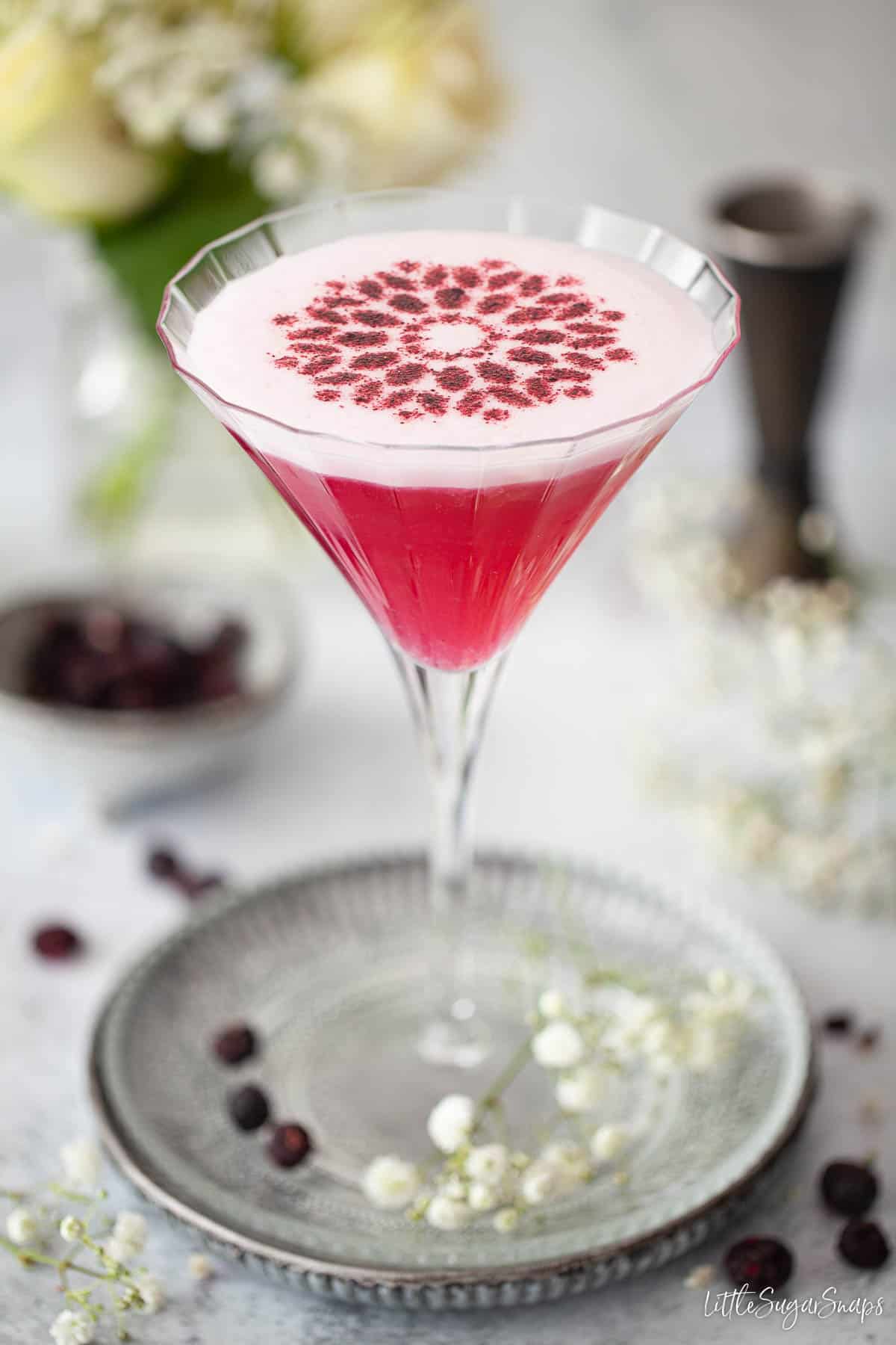 A blueberry cocktail garnished with a stencil made from blueberry powder.