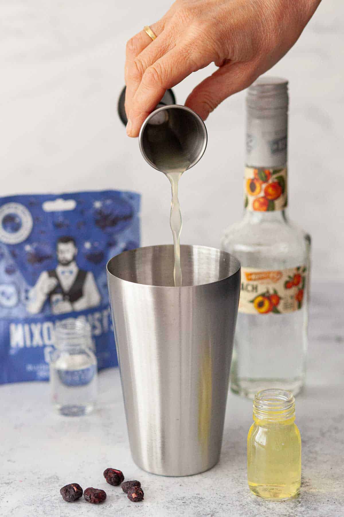 A person pouring lemon juice into a cocktail shaker.