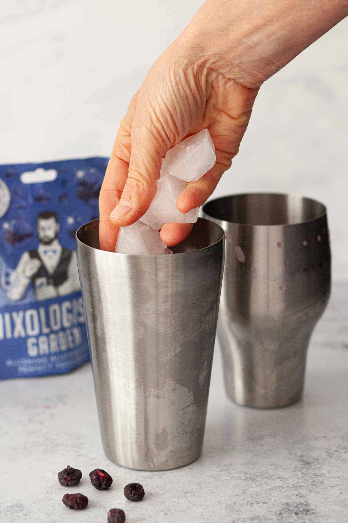 A person putting ice inside of a cocktail shaker.