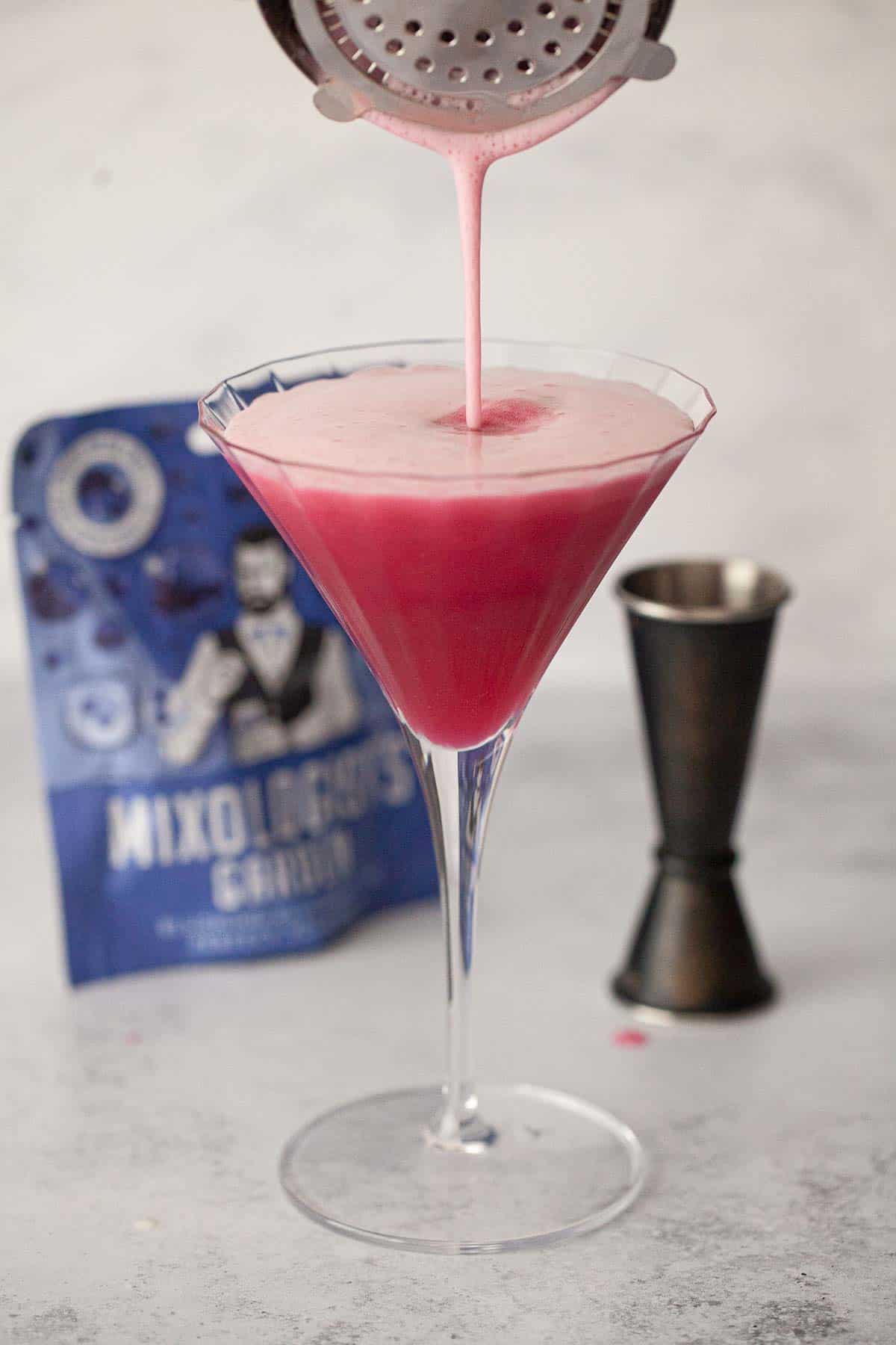 A pink cocktail being strained into a martini glass.