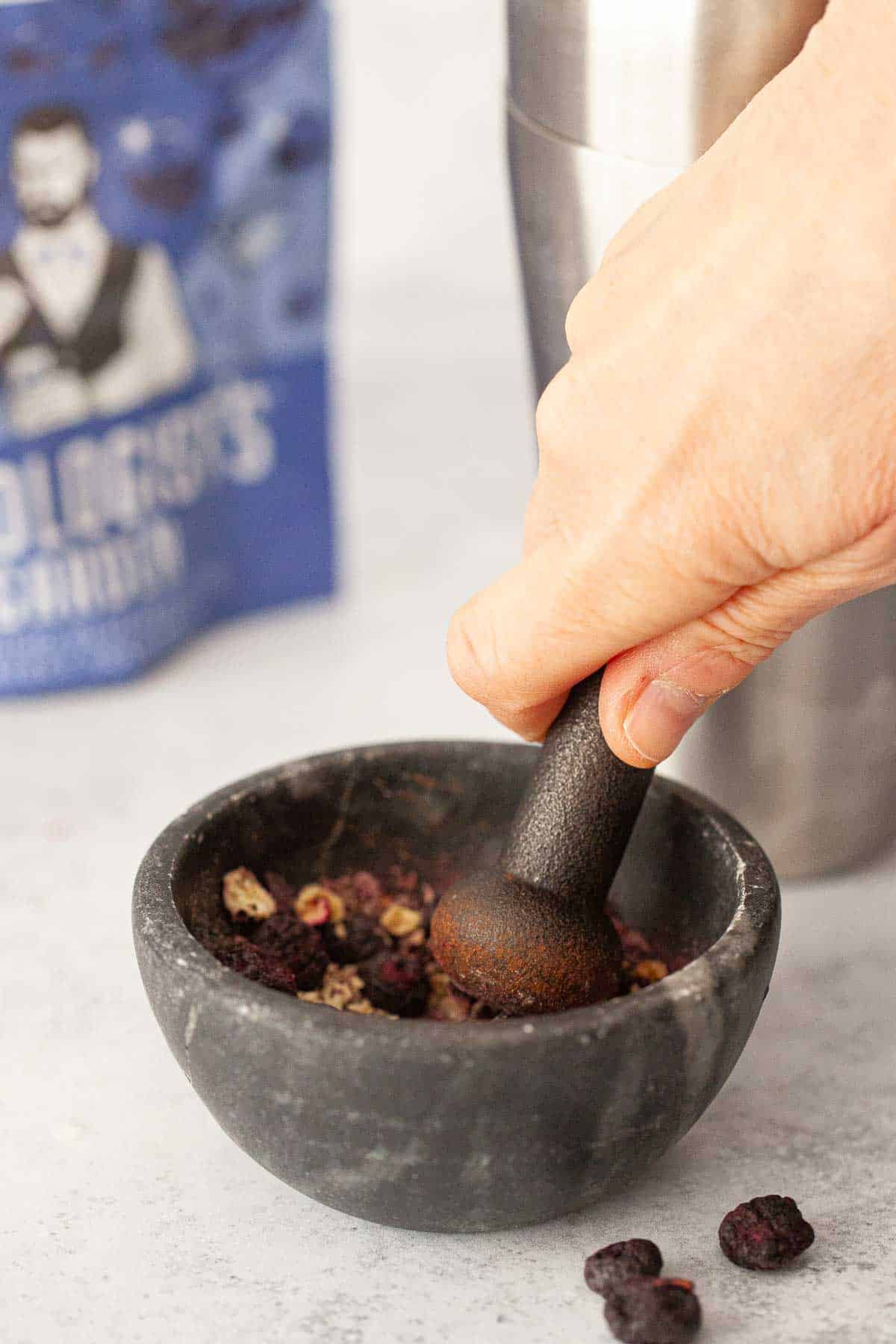 A person crushing freeze-dried blueberries with a pestle & mortar.