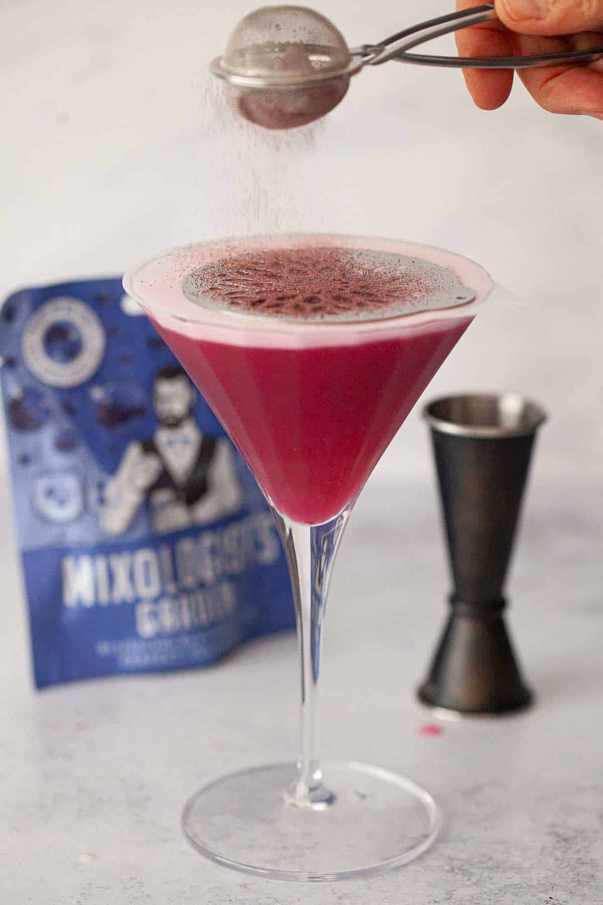 Blueberry powder being sieved over a cocktail.