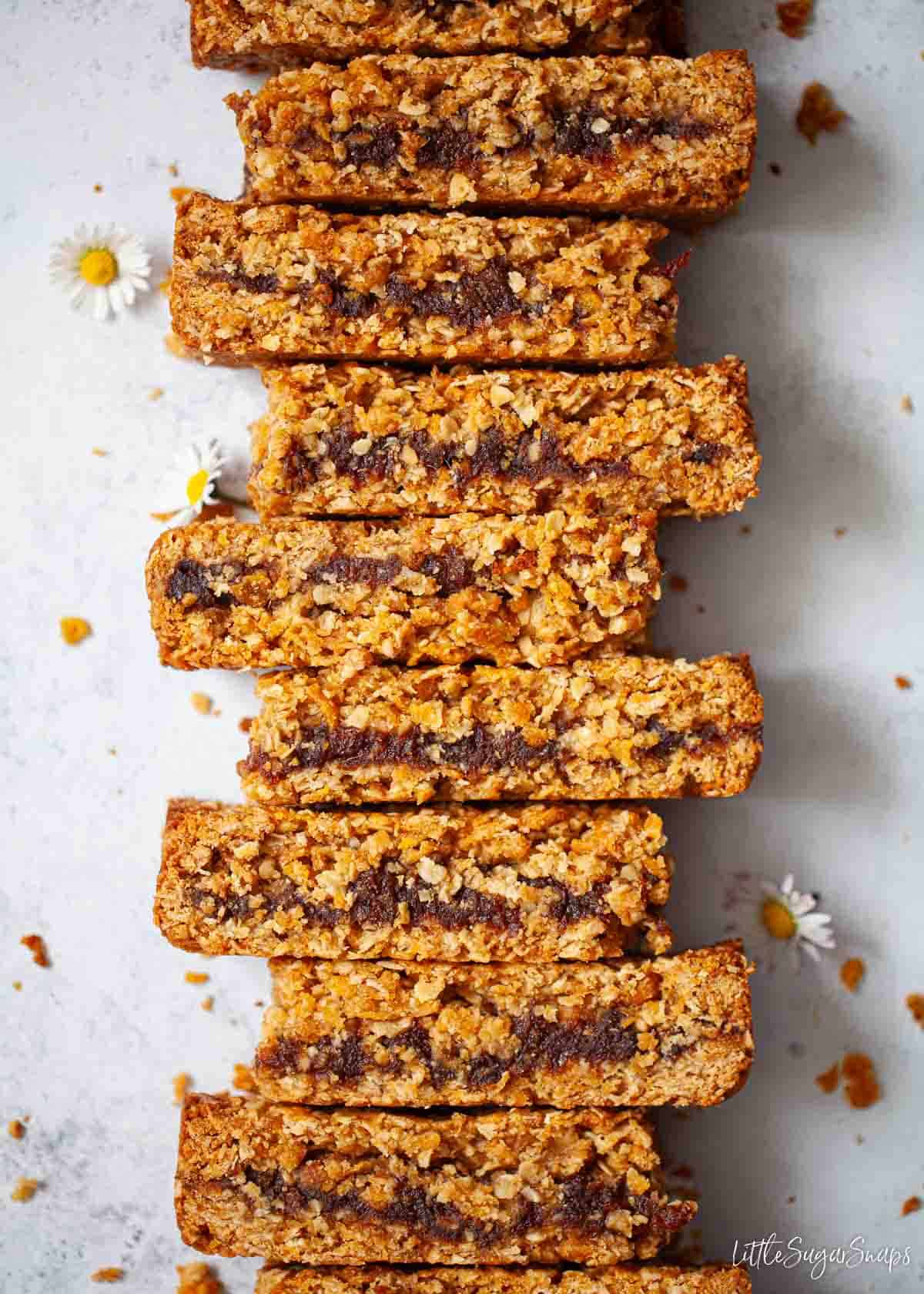 A row of sticky date slices with daisies on the worktop.