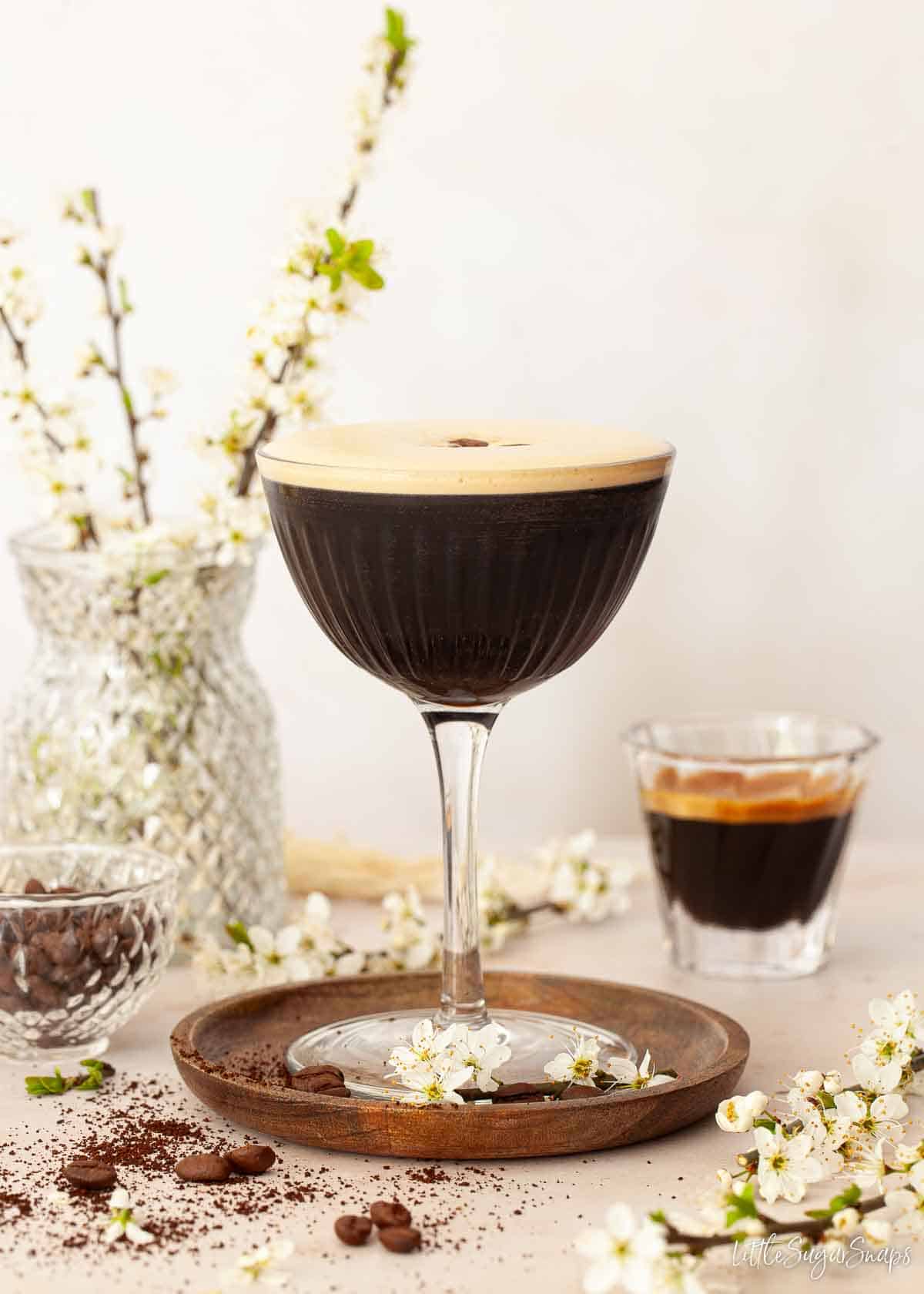 An espresoo gin martini with a shot of espresso coffee and white flowers alongsde.