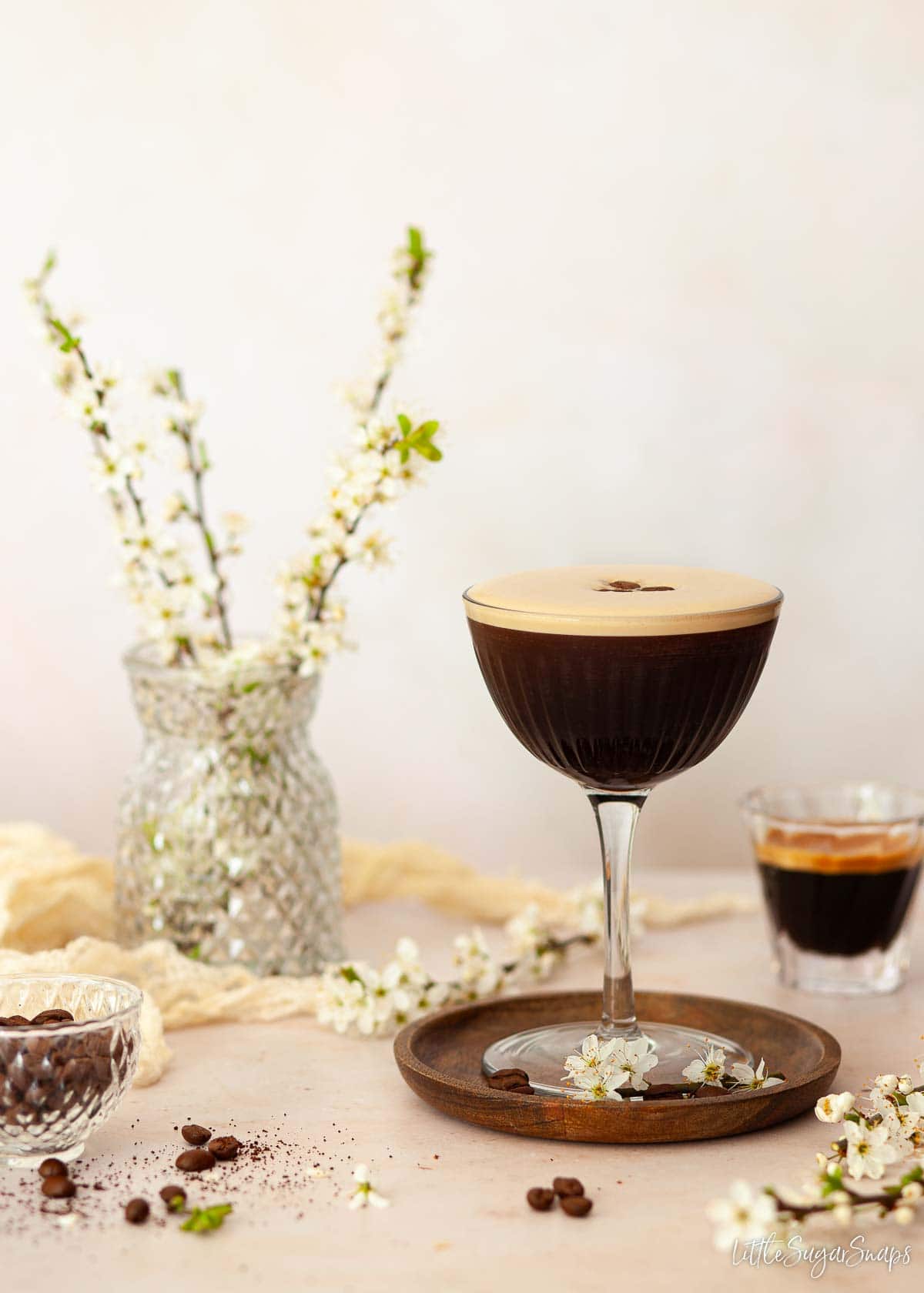 An espresso gin martini with a shot of espresso and flowers in the background.