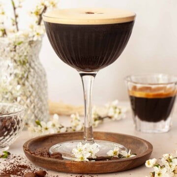 Close up of a gin espresso martini with an espresso shot and flowers in the background.