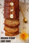 Overhead view of a sliced golden syrup loaf cake decorated with daisies with text overlay.