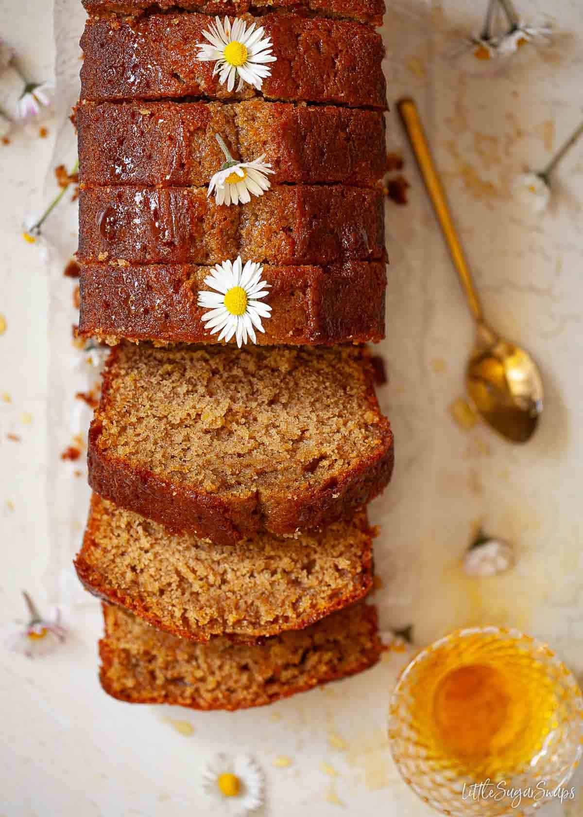 Overhead view of a sliced golden syrup loaf cake decorated with daisies.