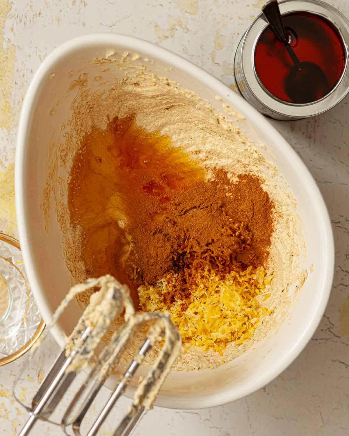 Golden syrup, lemon zest and ground cinnamon measured into a bowl of cake batter.