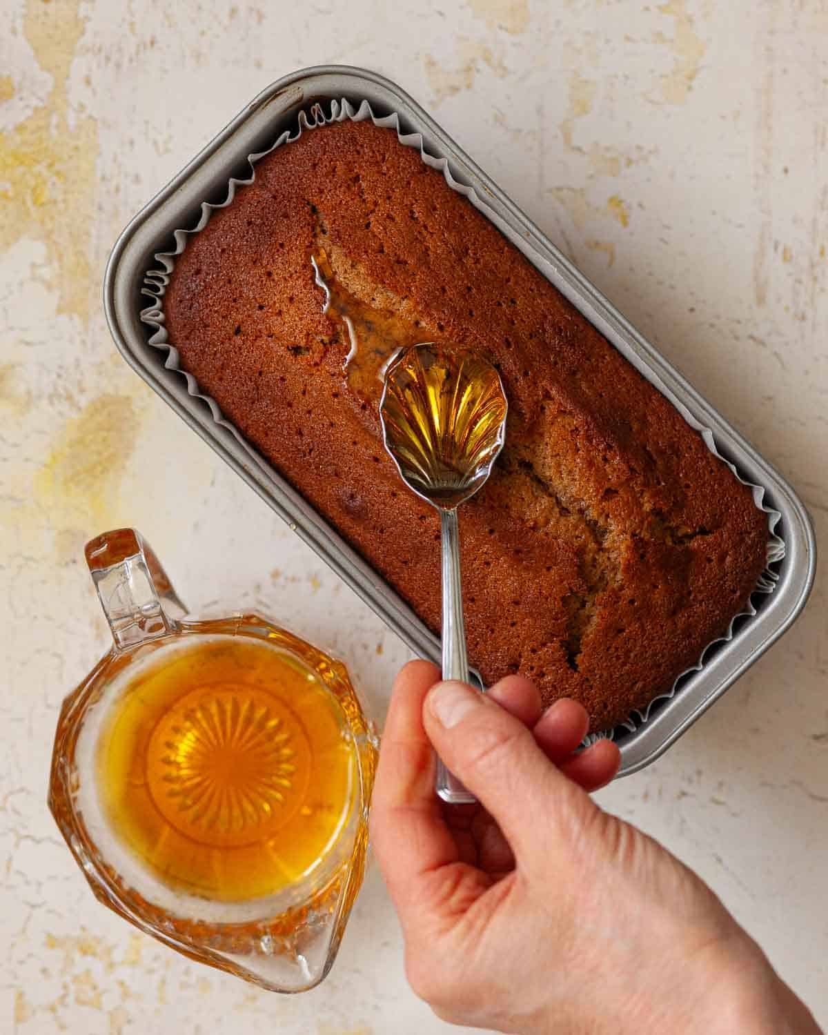 A person spooning syrup over the top of a loaf cake.