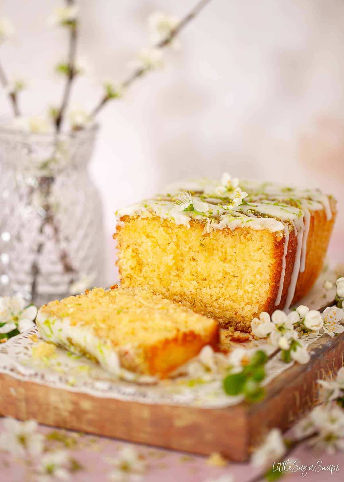 A part sliced lime drizzle cake with spring blossom garnish.