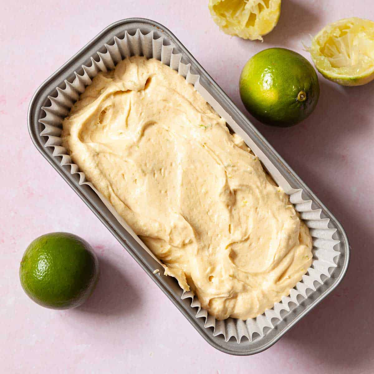 Cake batter in a loaf tin with limes next to the tin.