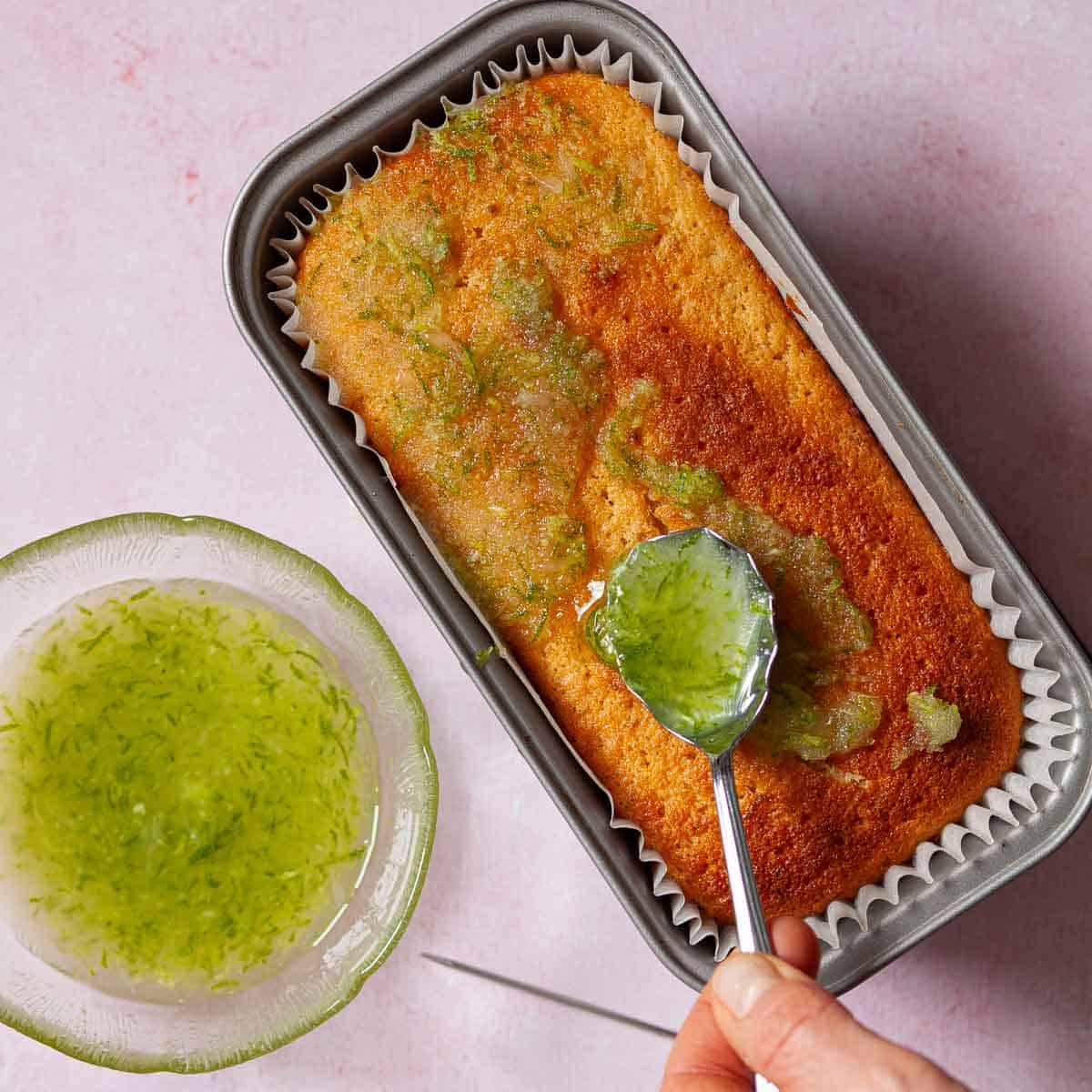 Lime syrup being spooned over a lime loaf cake.