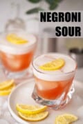 Two glasses of Negroni sour with egg white foam and lemon slice garnish. With text overlay.