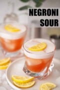 Two glasses of Negroni sour with egg white foam and lemon slice garnish. With text overlay.