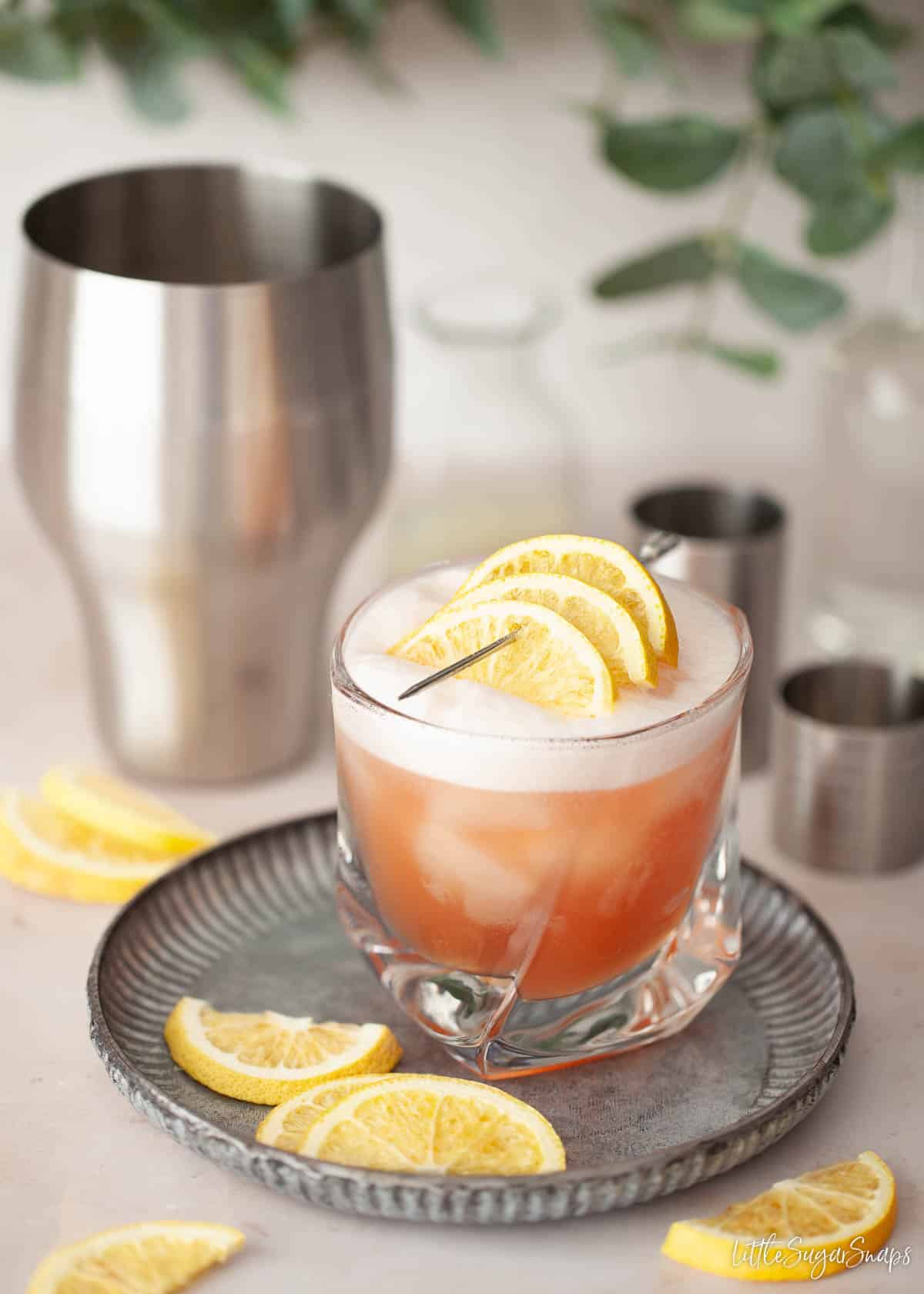 Gin Campari sour in a tumbler with egg white foam and lemon slices to garnish.