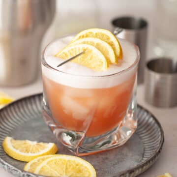 Close-up of a gin and campari sour garnished with three slices of lemon on a cocktail pick.